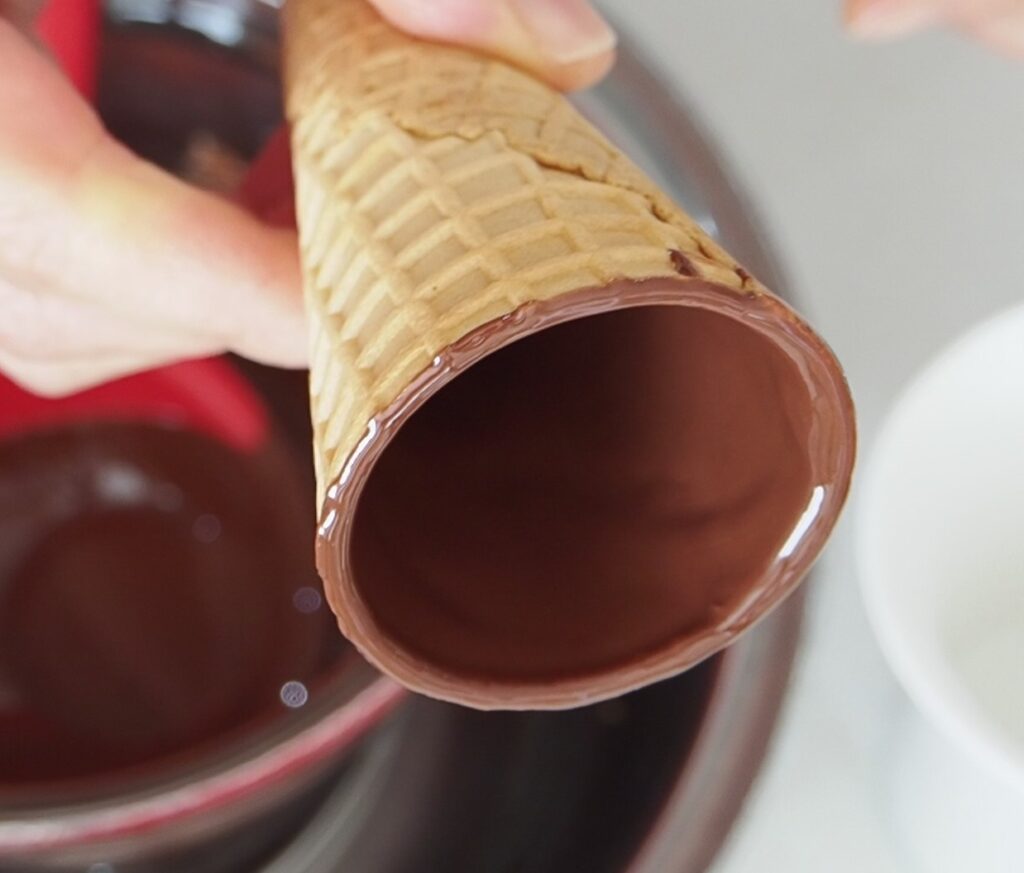 手順③　手順②をくり返し、全体にチョコレートが行き渡ったら、マグカップにコーンを入れ冷凍庫で10分ほど冷やす